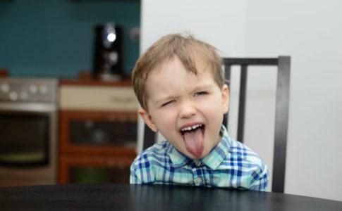Kind streckt frech die Zunge am Tisch raus