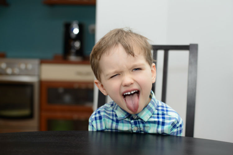 Kind streckt frech die Zunge am Tisch raus