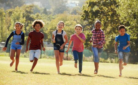 Kinder laufen barfuß und lachend über eine Wiese