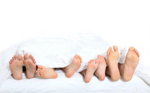 Fueße von Eltern und zwei Kindern, die gemeinsam in einem Familienbett schlafen