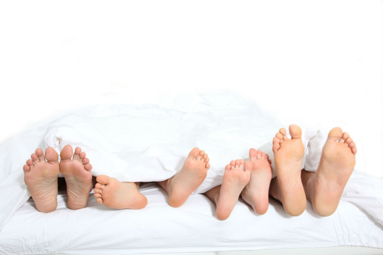 Fueße von Eltern und zwei Kindern, die gemeinsam in einem Familienbett schlafen