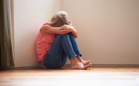 Ein junges Mädchen, das traurig am Boden sitzt