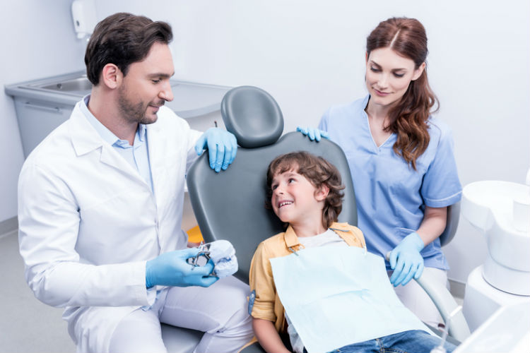 Kleiner Junge beim Kieferorthophaeden, dem etwas vom Arzt erklärt wird
