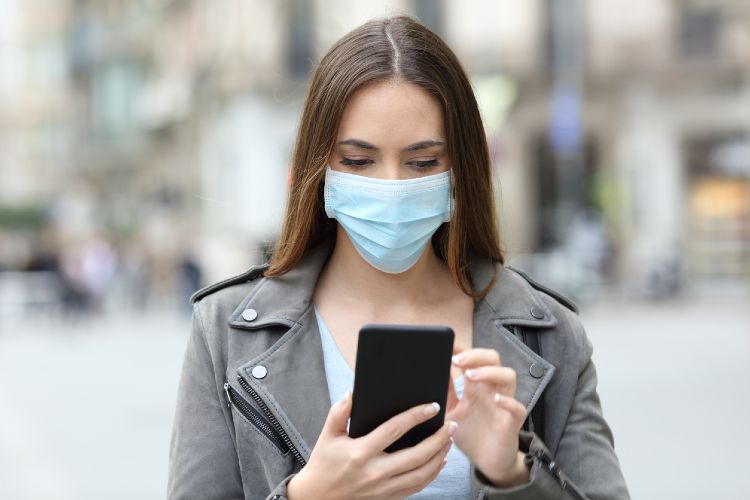 Frau mit Maske benutzt Handy