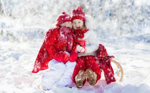 Zwei Kinder sitzen auf dem Schlitten und Lachen im Winter