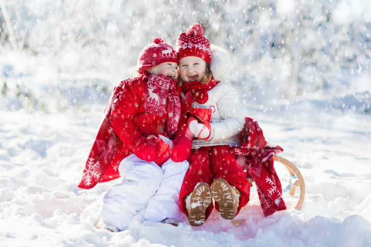 Zwei Kinder sitzen auf dem Schlitten und Lachen im Winter