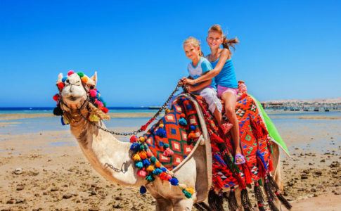 Zwei Mädchen reiten auf einem Kamel am Strand