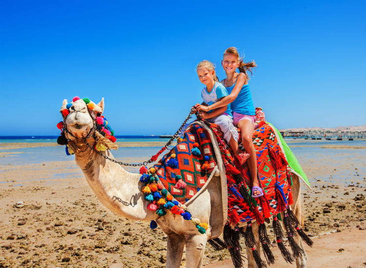 Zwei Mädchen reiten auf einem Kamel am Strand