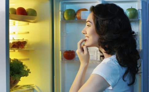 Frau steht vor dem Kühlschrank und überlegt was sie essen kann