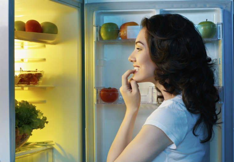 Frau steht vor dem Kühlschrank und überlegt was sie essen kann