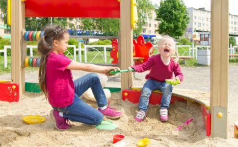 Geschwister die sich auf einem Spielplatz um eine Schaufel streiten