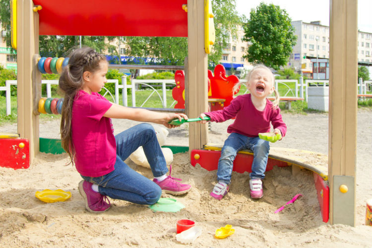 Geschwister die sich auf einem Spielplatz um eine Schaufel streiten