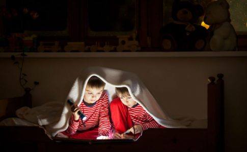 Geschwister lesen in einem gemeinsamen Zimmer unter der Decke