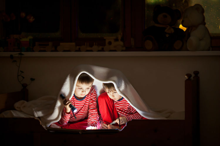 Geschwister lesen in einem gemeinsamen Zimmer unter der Decke
