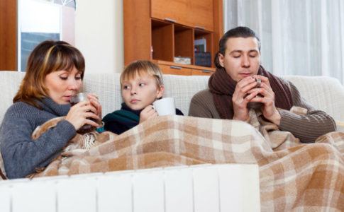 Eine Familie, die erkältet zusammen auf dem Sofa liegt und Tee trinkt