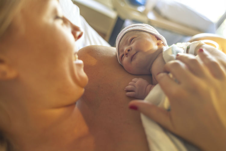 Frau lächelt frisch geborenes Baby an, das sie im Arm hält