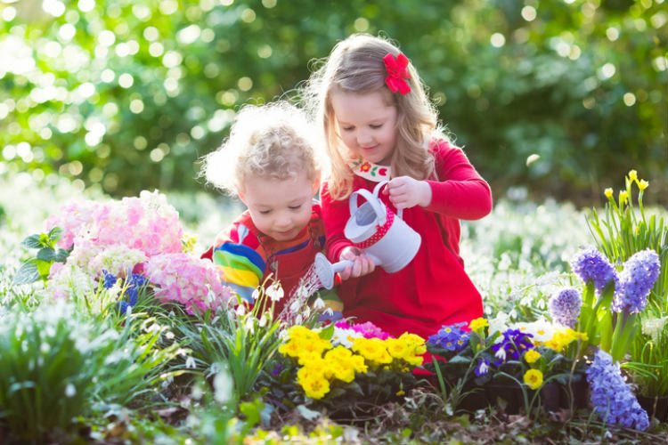 Kinder in Blumenbeet am Blumen gießen - Lieblingsplatz im Garten