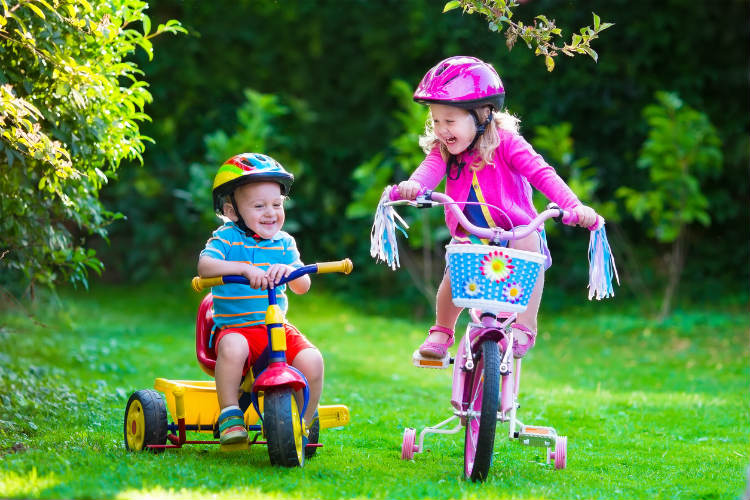 Kinderfahrzeug - Jnge auf Dreirad und Mädchen auf Fahrrad im Garten