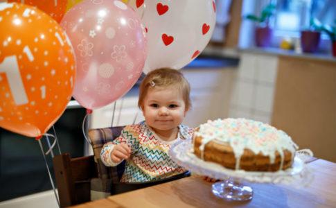Kleines Mädchen mit Geburtstagskuchen und Ballons, auf denen eine 1 steht