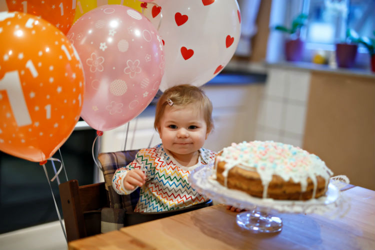 Kleines Mädchen mit Geburtstagskuchen und Ballons, auf denen eine 1 steht
