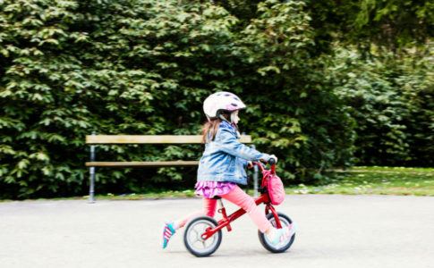 Kleines Mädchen mit Helm, das auf einem Laufrad Fahrradfahren lernt