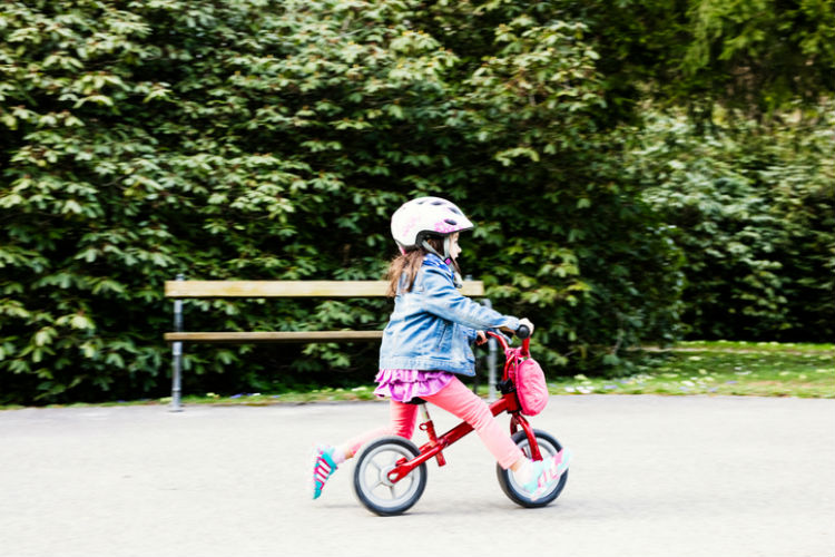 Kleines Mädchen mit Helm, das auf einem Laufrad Fahrradfahren lernt
