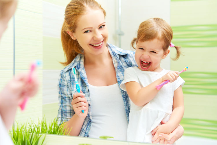 Glückliche Mutter putzt mit ihrem glücklichen Kind die Zähne mit Zahnbürsten