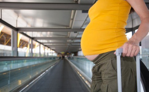 schwanger Frau zieht einen Koffer in Flughafen