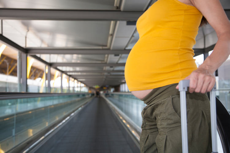 schwanger Frau zieht einen Koffer in Flughafen