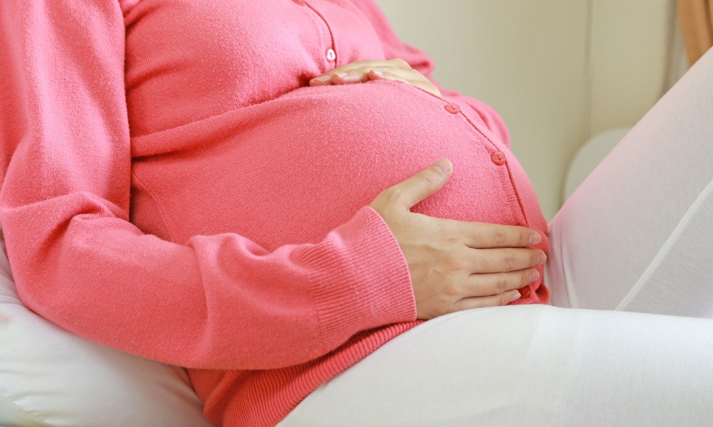 Schwangere Frau in Strickjacke streichelt Bauch