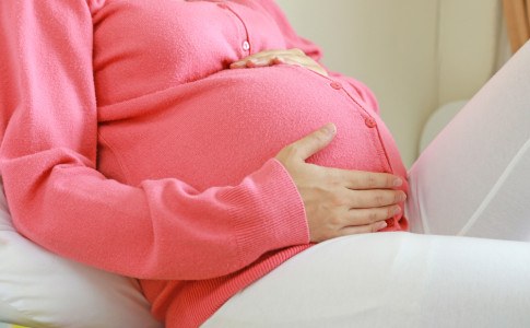 Schwangere Frau in Strickjacke streichelt Bauch