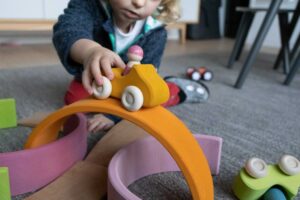 Ein Kind spielt mit einem aus Holz gefertigten Spielzeugauto