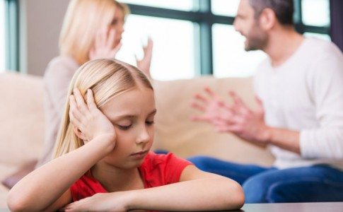 Betrübtes Kind im Fokus mit streitenden Eltern im Hintergrund