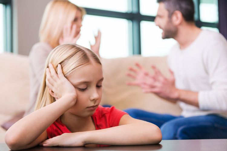 Betrübtes Kind im Fokus mit streitenden Eltern im Hintergrund