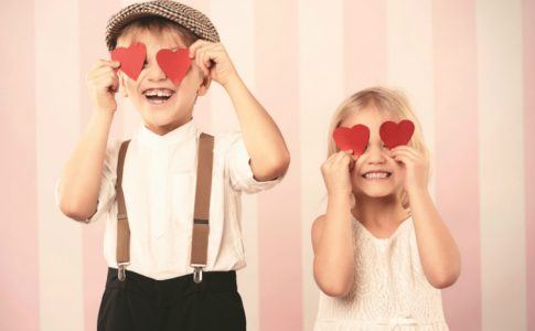 Einen schönen Valentinstag mit der Familie - zwei Kinder halten sich rote Papierherzen vor die Augen