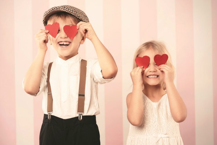 Einen schönen Valentinstag mit der Familie - zwei Kinder halten sich rote Papierherzen vor die Augen