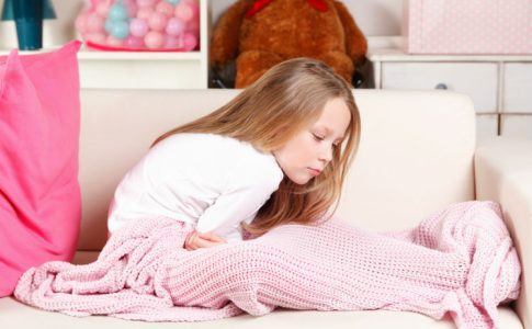 Mädchen sitzt auf Bett und hält sich den Bauch vor Schmerzen