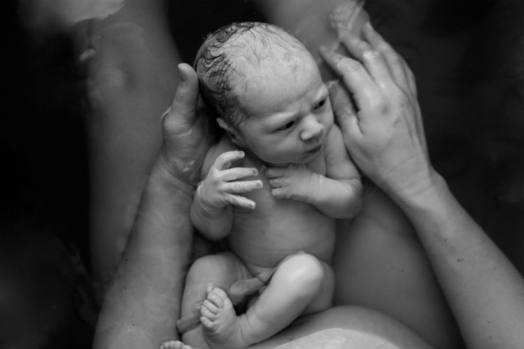 Mutter hält Neugeborenes nach Wassergeburt im Becken auf dem Arm