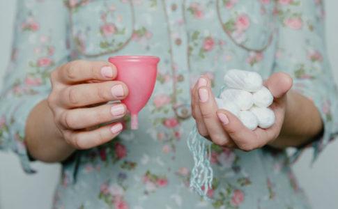 Eine Frau haelt Tampons und eine Menstruationstasse in den Haenden