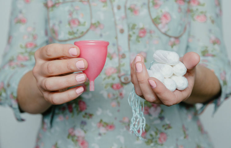 Eine Frau haelt Tampons und eine Menstruationstasse in den Haenden