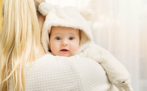 Mutter trägt Baby auf dem Arm, das warm angezogen ist