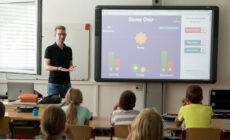 Ein Lehrer steht vor einem Smartboard und unterrichtet
