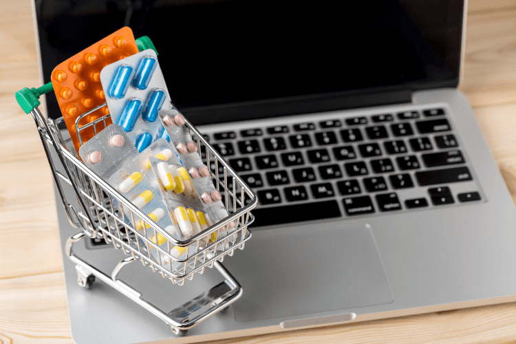 Kleiner Einkaufswagen mit verschiedenen Medikamenten auf einem Notebook
