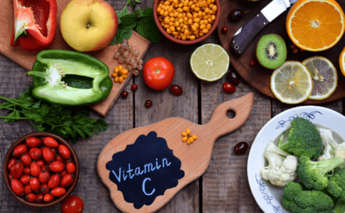 Verschieden Obst- und Gemüsesorten und ein Brett mit der Aufschrift Vitamin C auf einer Holzunterlage