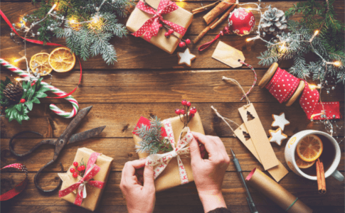 Zwei Hände, die ein Geschenk einpacken auf einem weihnachtlich dekorierten Tisch