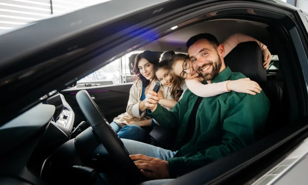 Familie im Auto, Vater hält Autoschlüssel, Kinder umarmen ihn auf dem Fahrersitz.