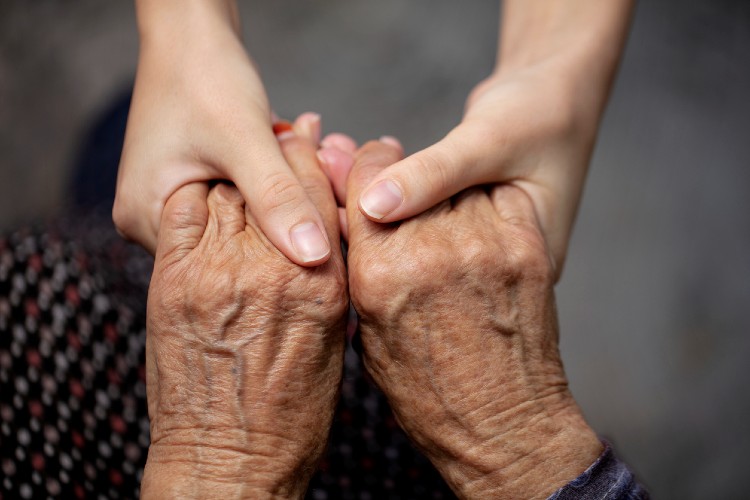 Zwei Menschen halten sich gegenseitig an den Händen. Eine Person älter, die andere deutlich jünger.