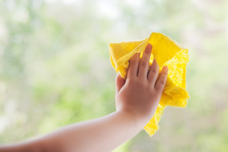 Eine Person putzt ein Fenster mit einem gelben Lappen