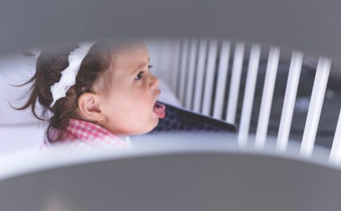 Ein Mädchen sitzt aufrecht im Kinderbett und hustet