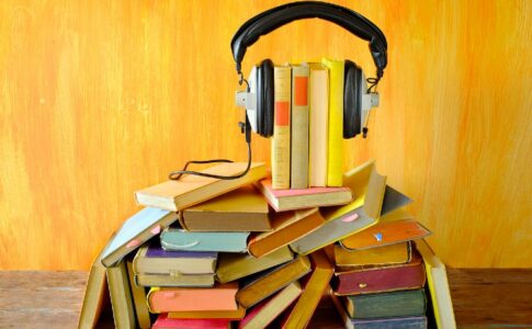 Mehrere Bücher sind übereinander gestapelt. Kopfhörer sind an den Büchern angebracht.